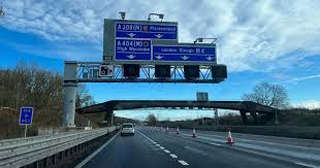 A car driving on a highway in California approaching a large overhead road sign with directions for upcoming exits under a partly cloudy sky.