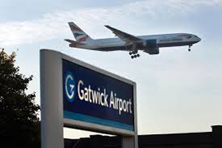 An airplane approaches for landing above the sign of Gatwick Airport during dusk.