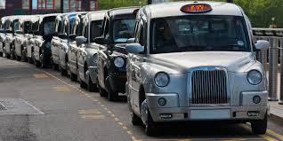 A row of traditional London black cabs lined up on a bustling city street.