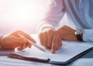 Close-up of an insurance agent's hands reviewing a document with a pen, suggesting an office or administrative setting.